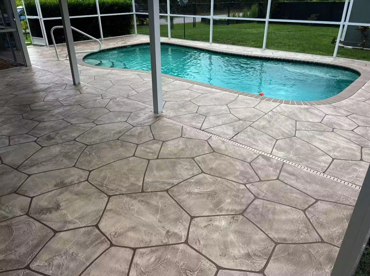 Stamped concrete pool deck with stone pattern, integral color, and decorative borders surrounding in-ground pool