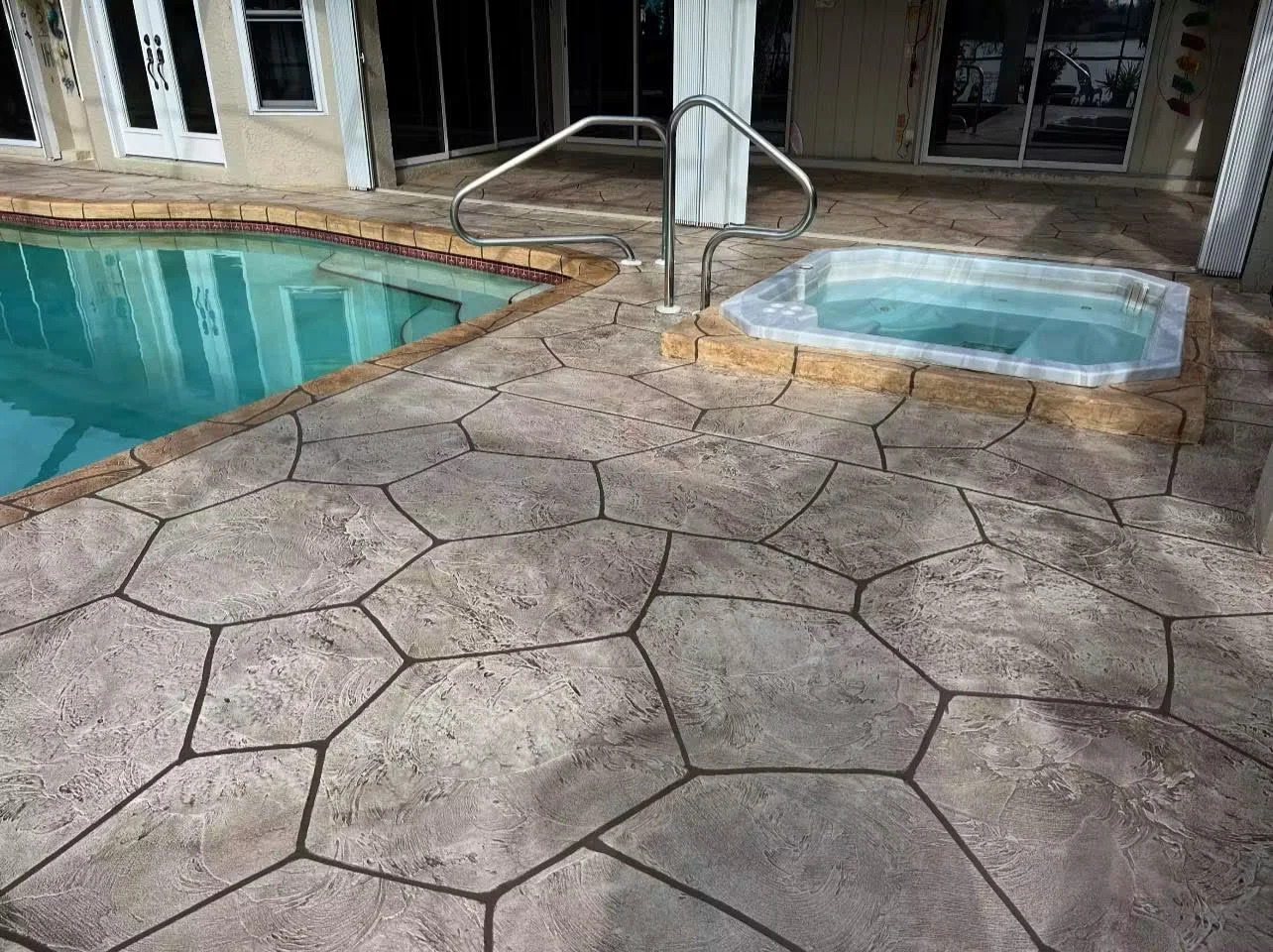 Stamped concrete pool deck with flagstone pattern and dark joints surrounding pool and spa
