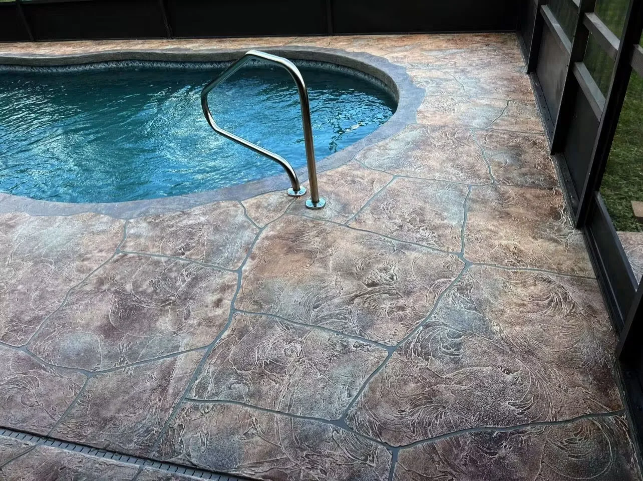 Stamped concrete pool deck with swirl pattern and metal pool handrail
