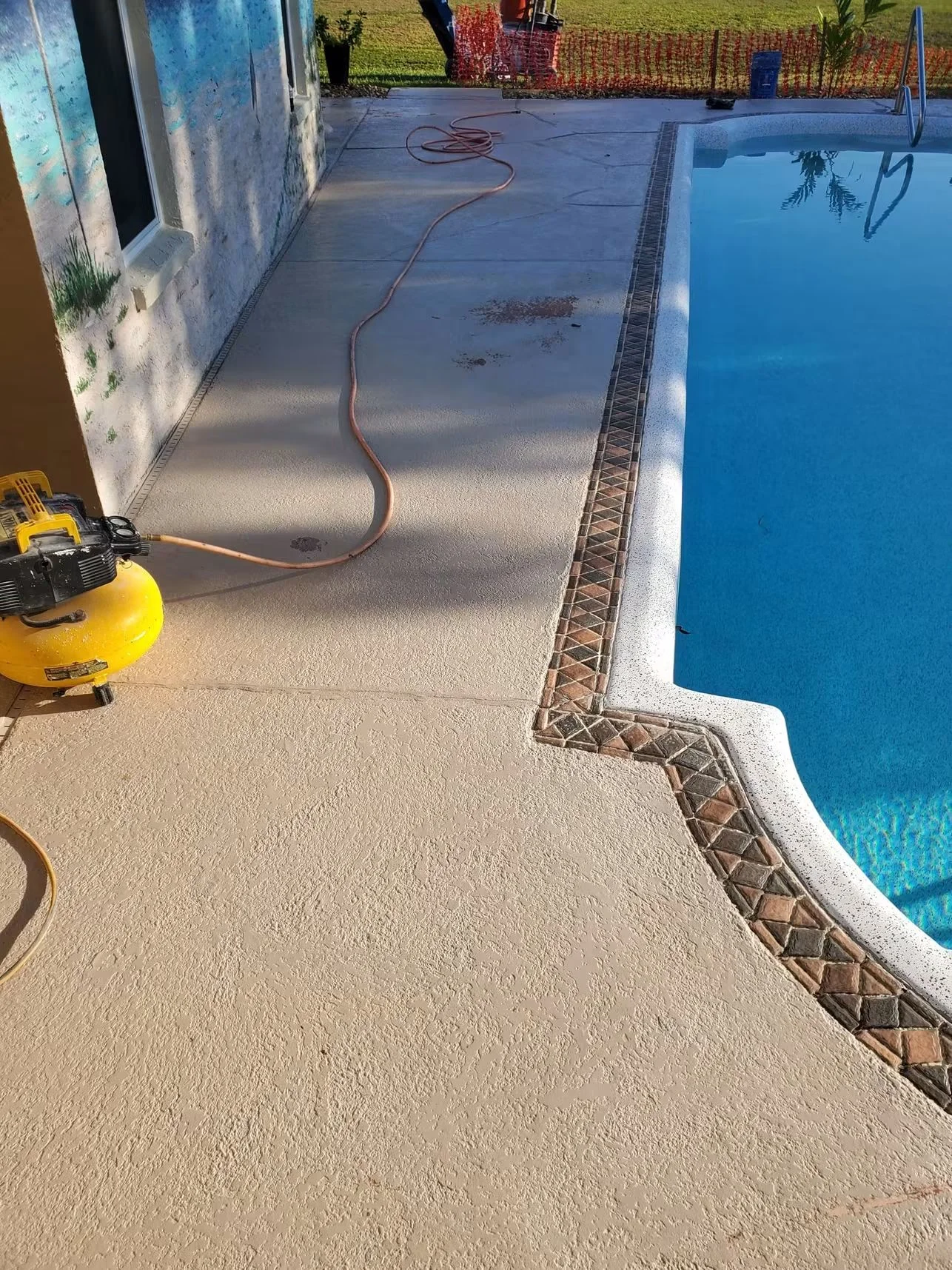 Concrete pool deck being pressure washed with decorative brick border trim visible