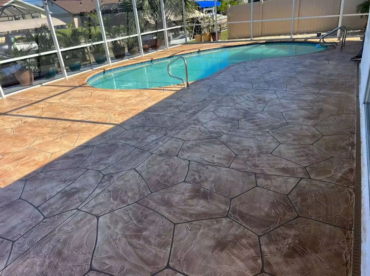 Stamped concrete pool deck with slate gray and tan stone pattern around swimming pool