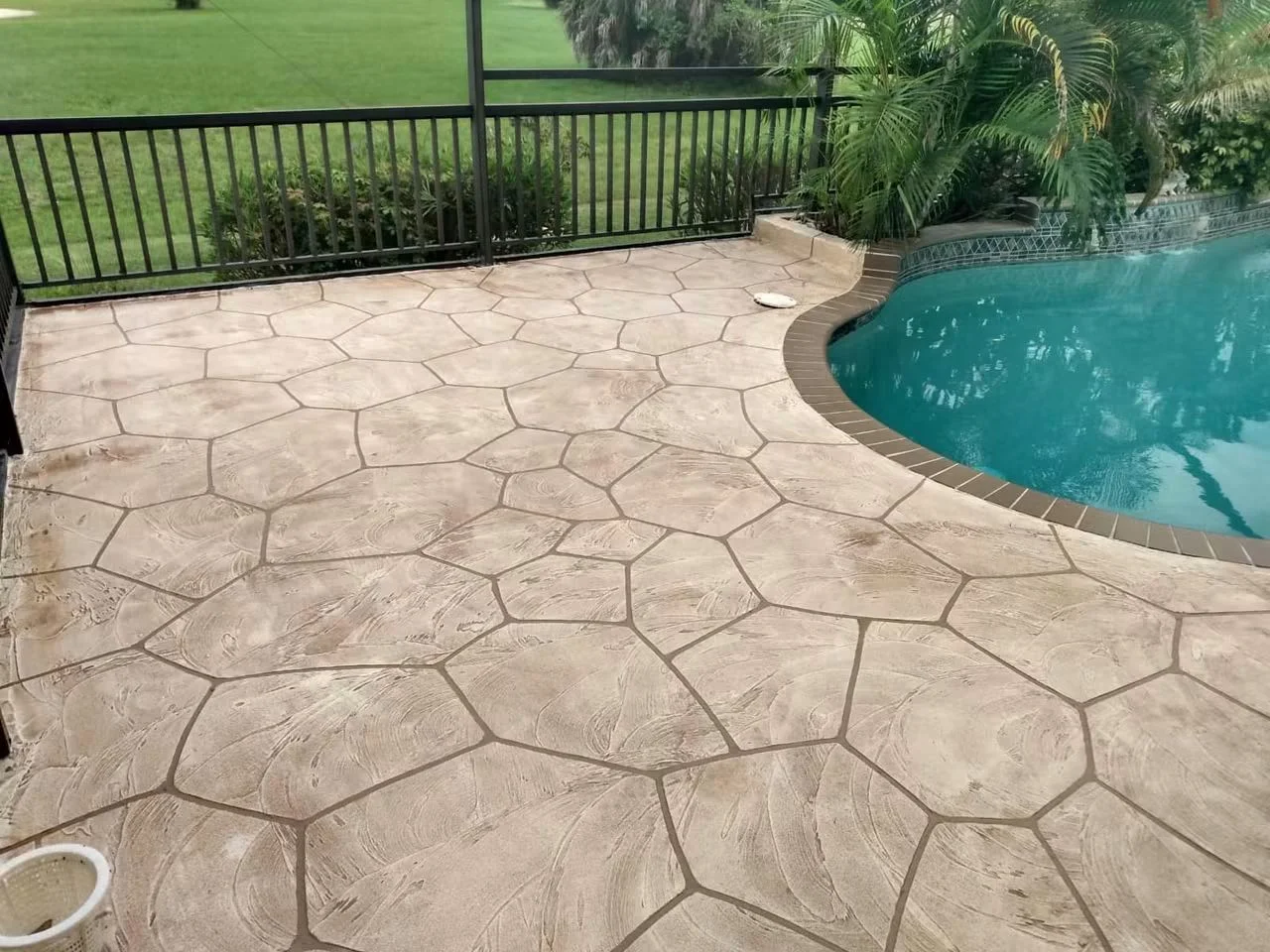 Stamped concrete pool deck with stone pattern and wood-grain texture around curved pool edge